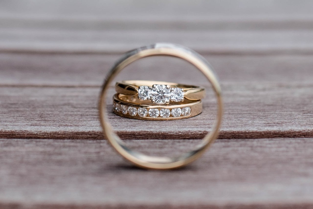 A wedding band and engagement ring set sitting on a wooden walkway.
