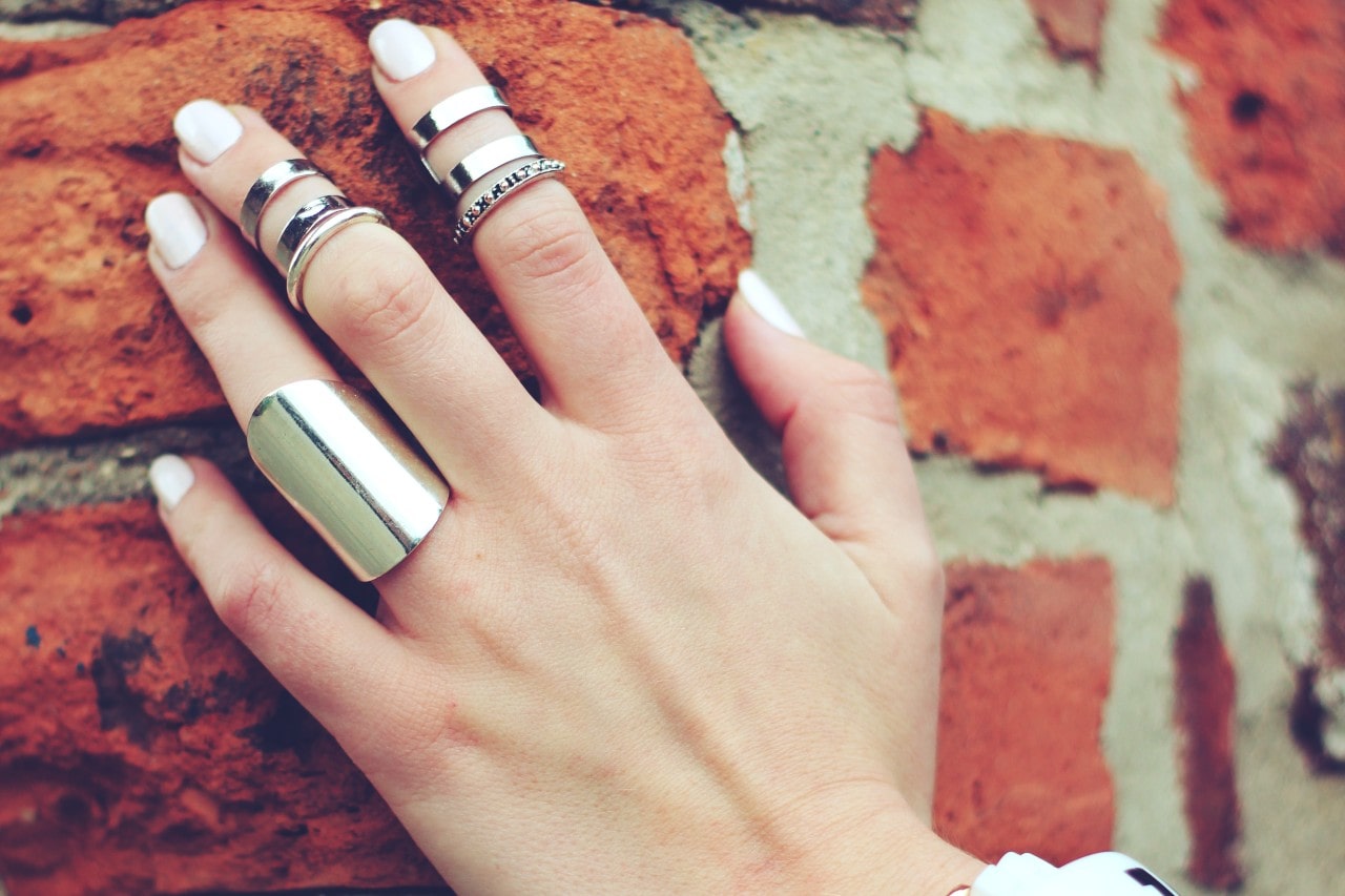 A close-up of a woman’s hand on a brick wall, adorned with many shining rings.