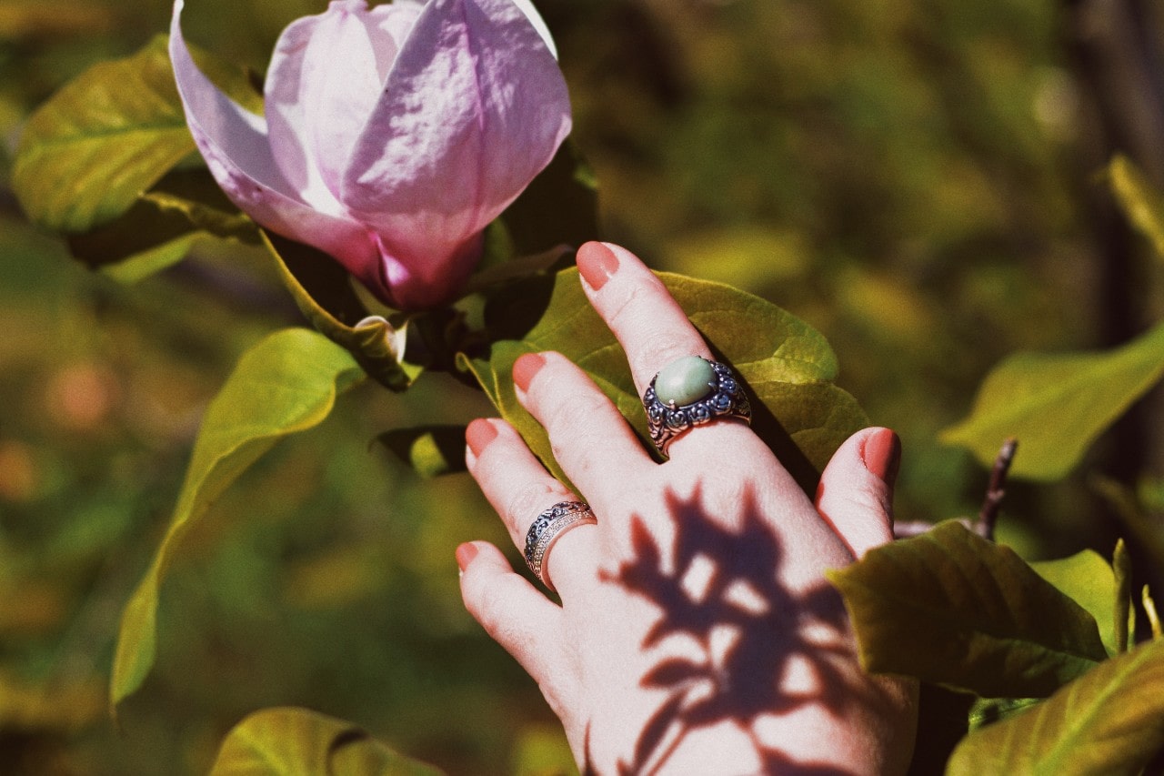 A close-up of a woman’s hand reaching for a flower, adorned with a simple yet elegant ring stack.