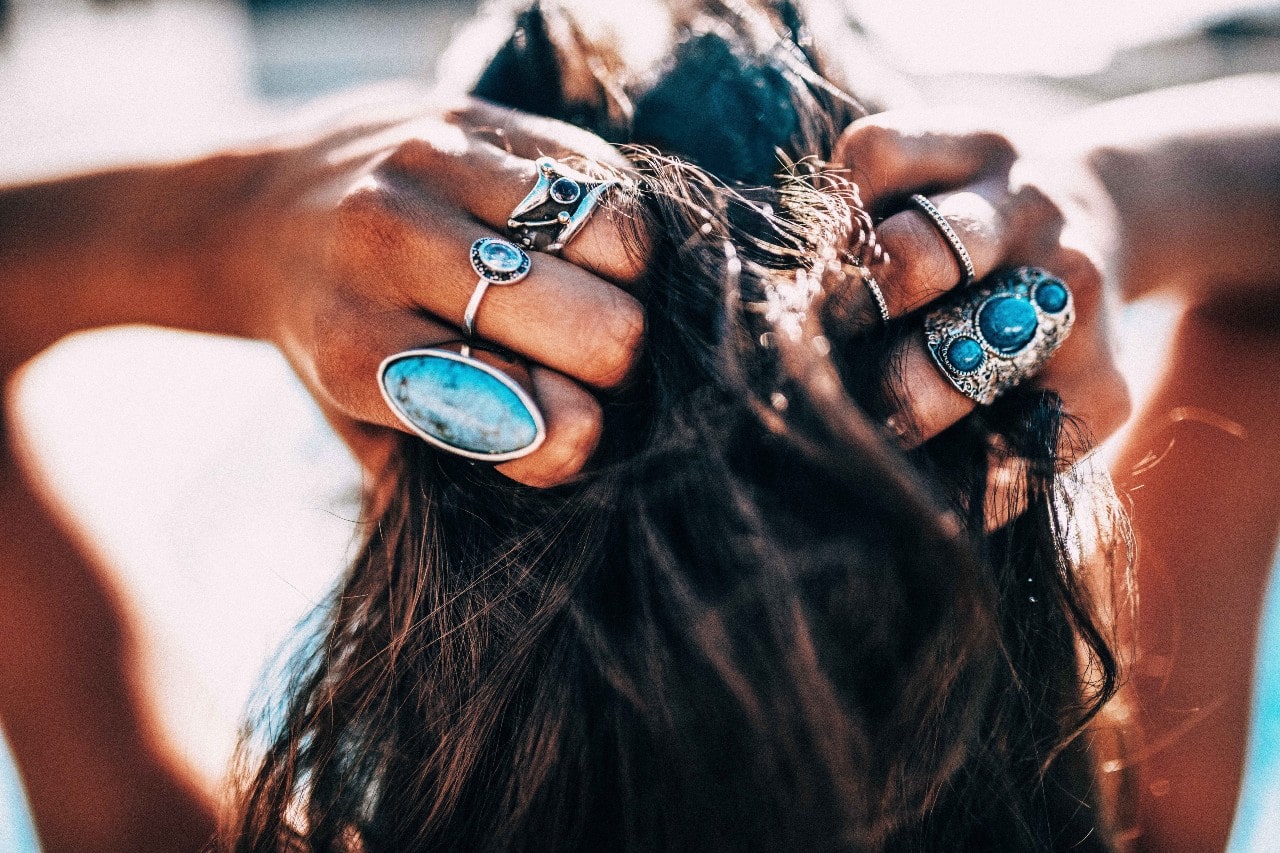 A close-up of a woman running her hands, adorned in beautiful rings, through her hair.