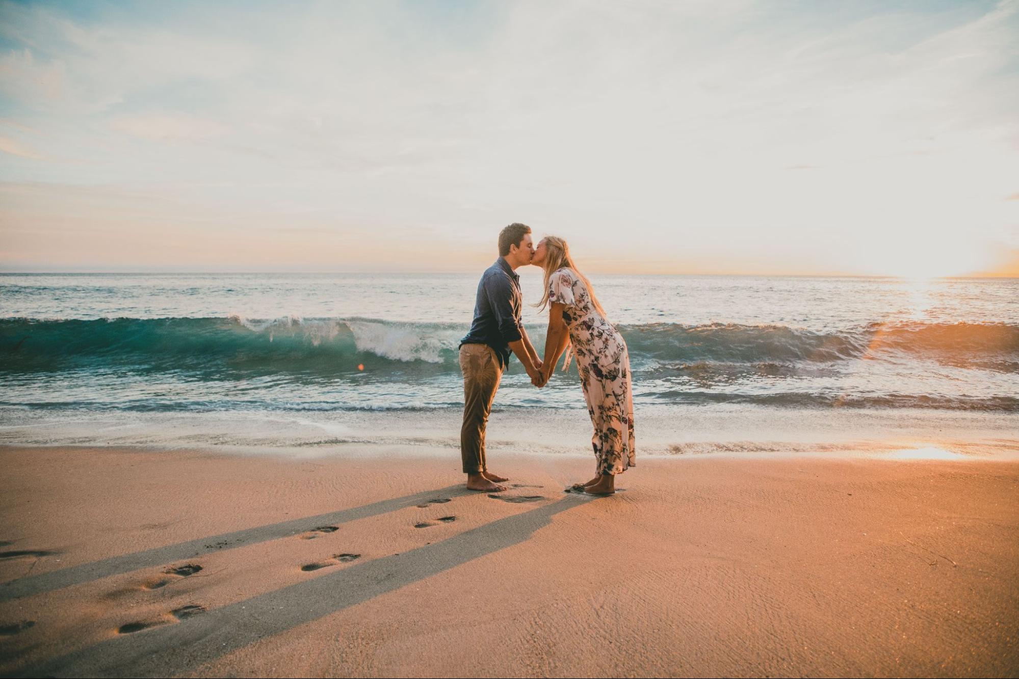 a couple kissing on a beach, the woman in a floral dress, the man in a blue shirt