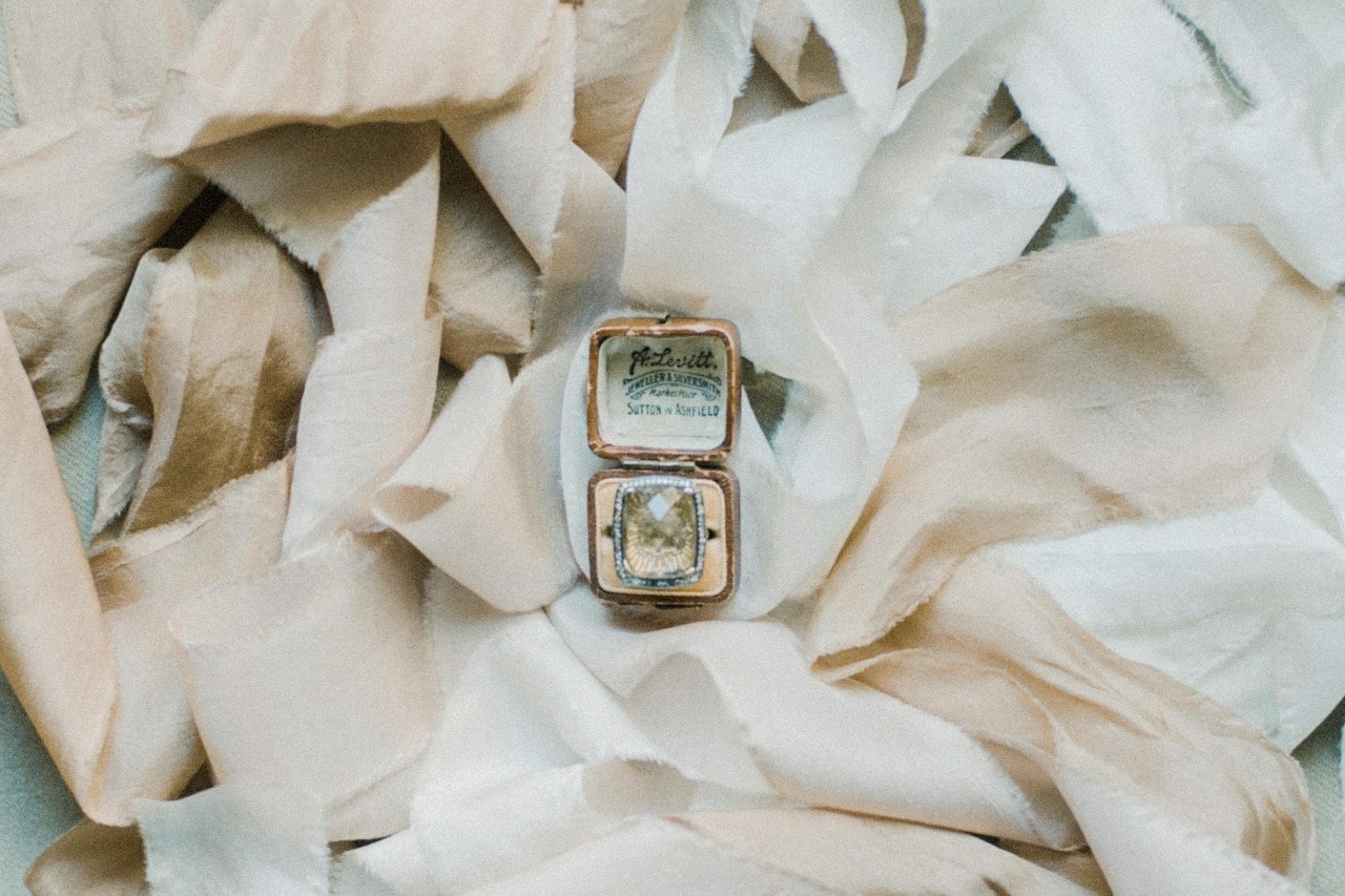 A ring box containing a large gemstone ring, displayed atop pale strips of fabric.