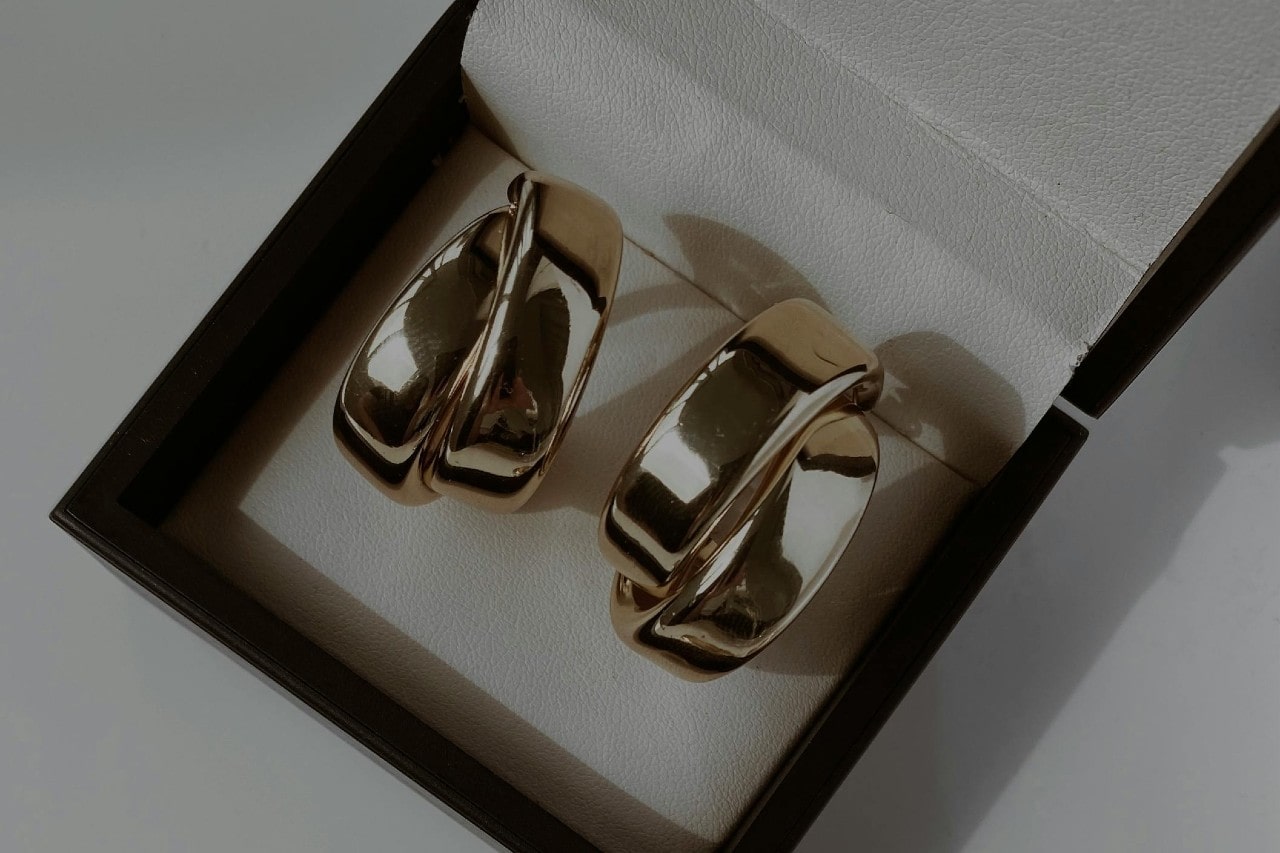 A black jewelry box holding a pair of sculptural yellow gold earrings.