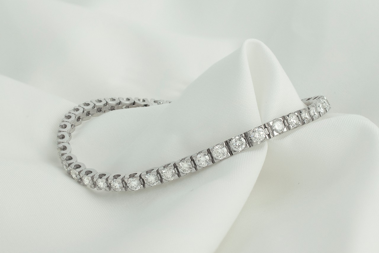 A close-up of a dazzling tennis bracelet displayed on a delicate white fabric backdrop.