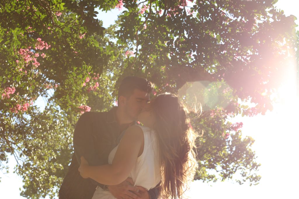 A couple kissing with a sunlit coastal view and trees in the background.