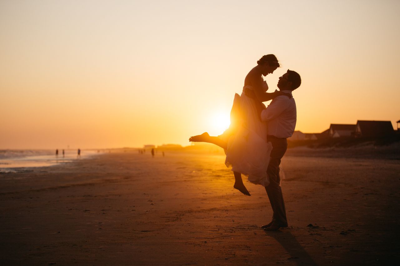 A couple embracing in front of the sunset on the beach.
