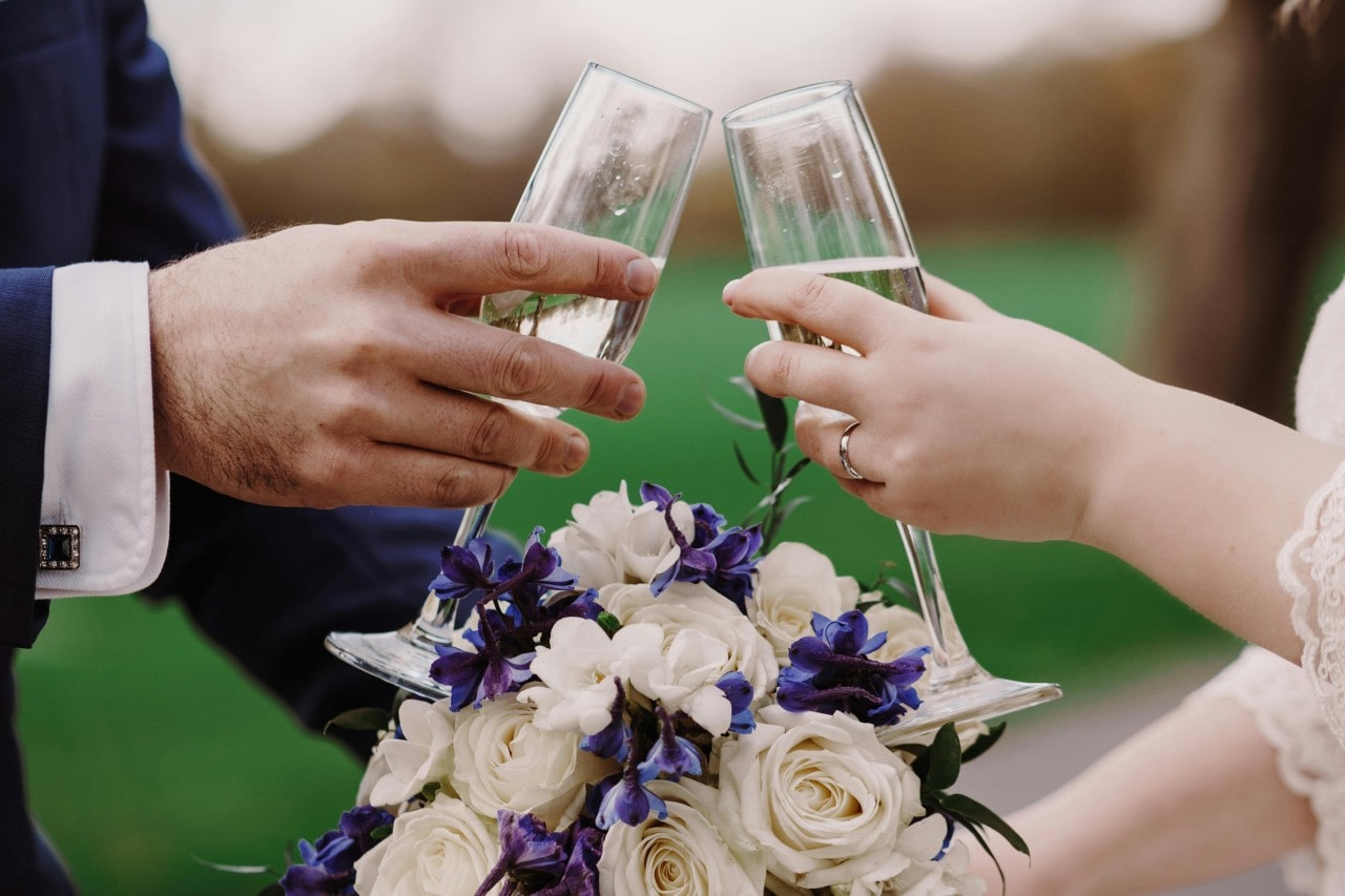 A couple cheering their champagne glasses over the top of a beautiful bouquet.