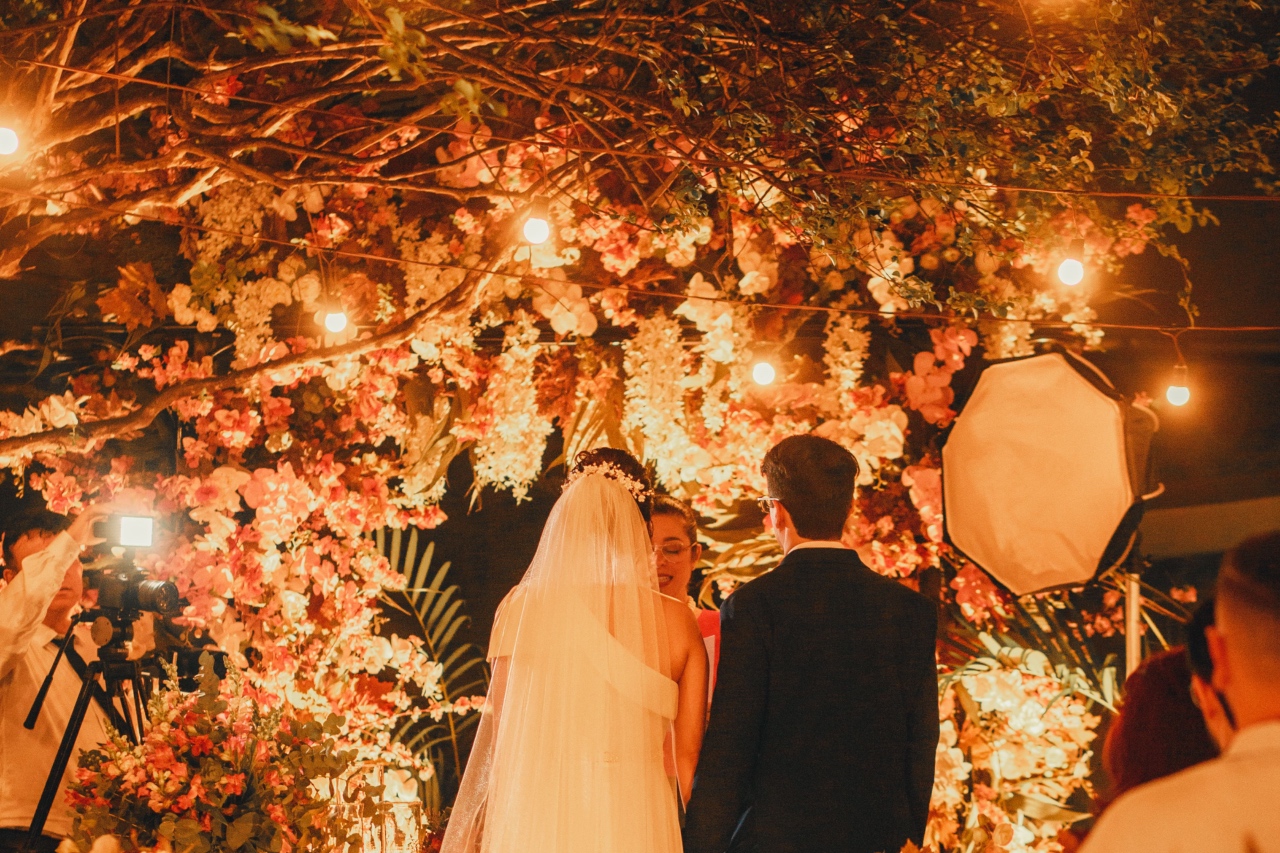 A close-up of the bride and groom standing at the altar, decorated with lots of flowers and lightbulbs while a photographer is taking their pictures from the side.