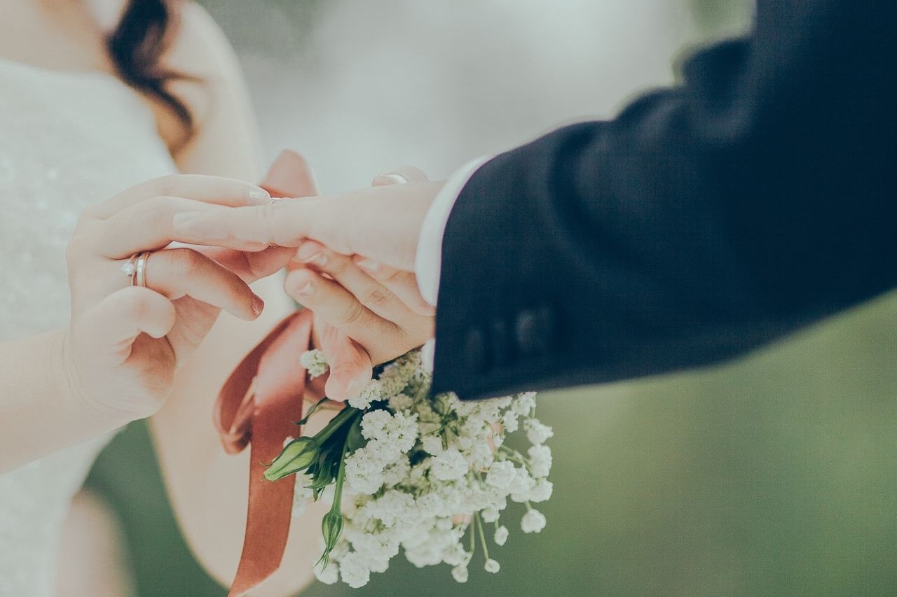 A close-up of a bride placing a ring on the groom's finger while holding a bouquet of white flowers. A close-up of a bride placing a ring on the groom's finger while holding a bouquet of white flowers.