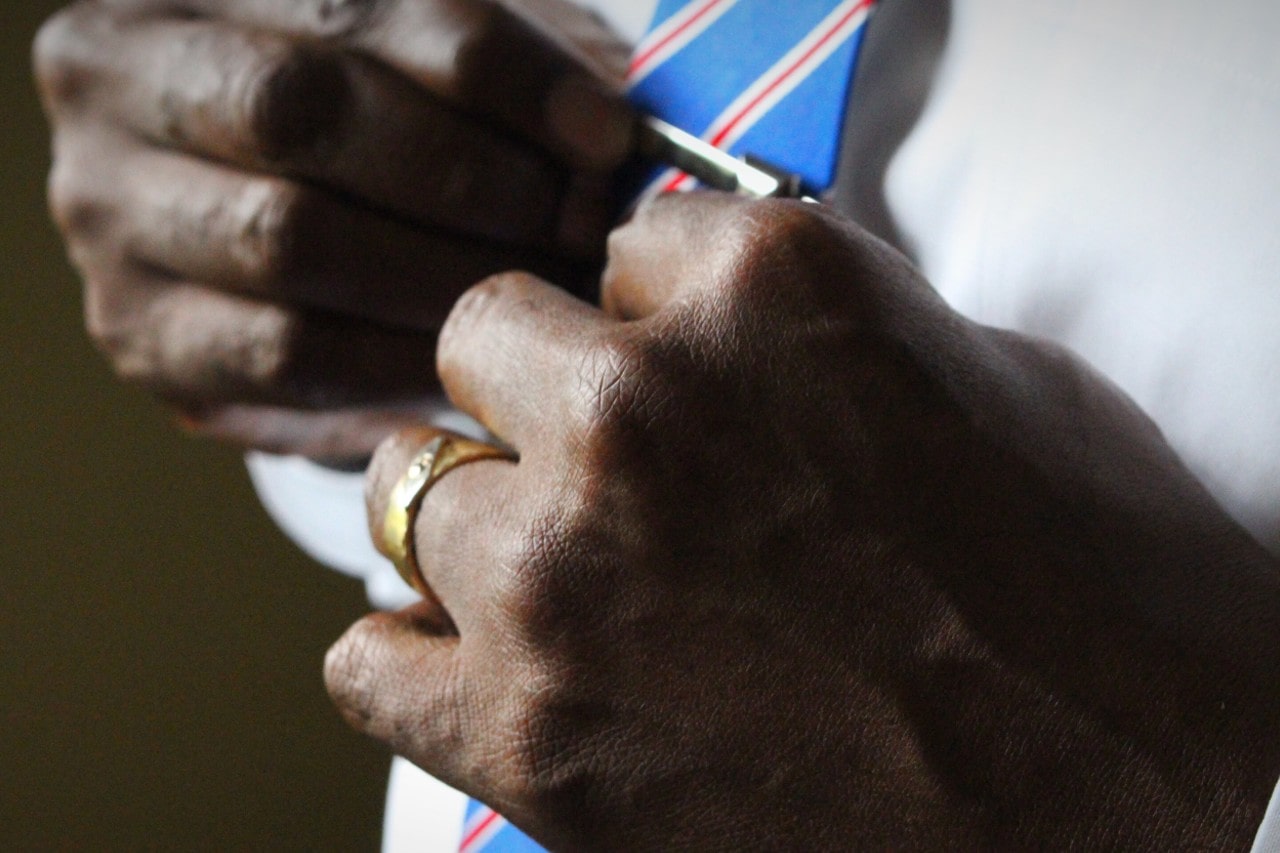 A close-up of a man wearing a gold ring, adjusting his blue tie with red and white stripes. A close-up of a man wearing a gold ring, adjusting his blue tie with red and white stripes.