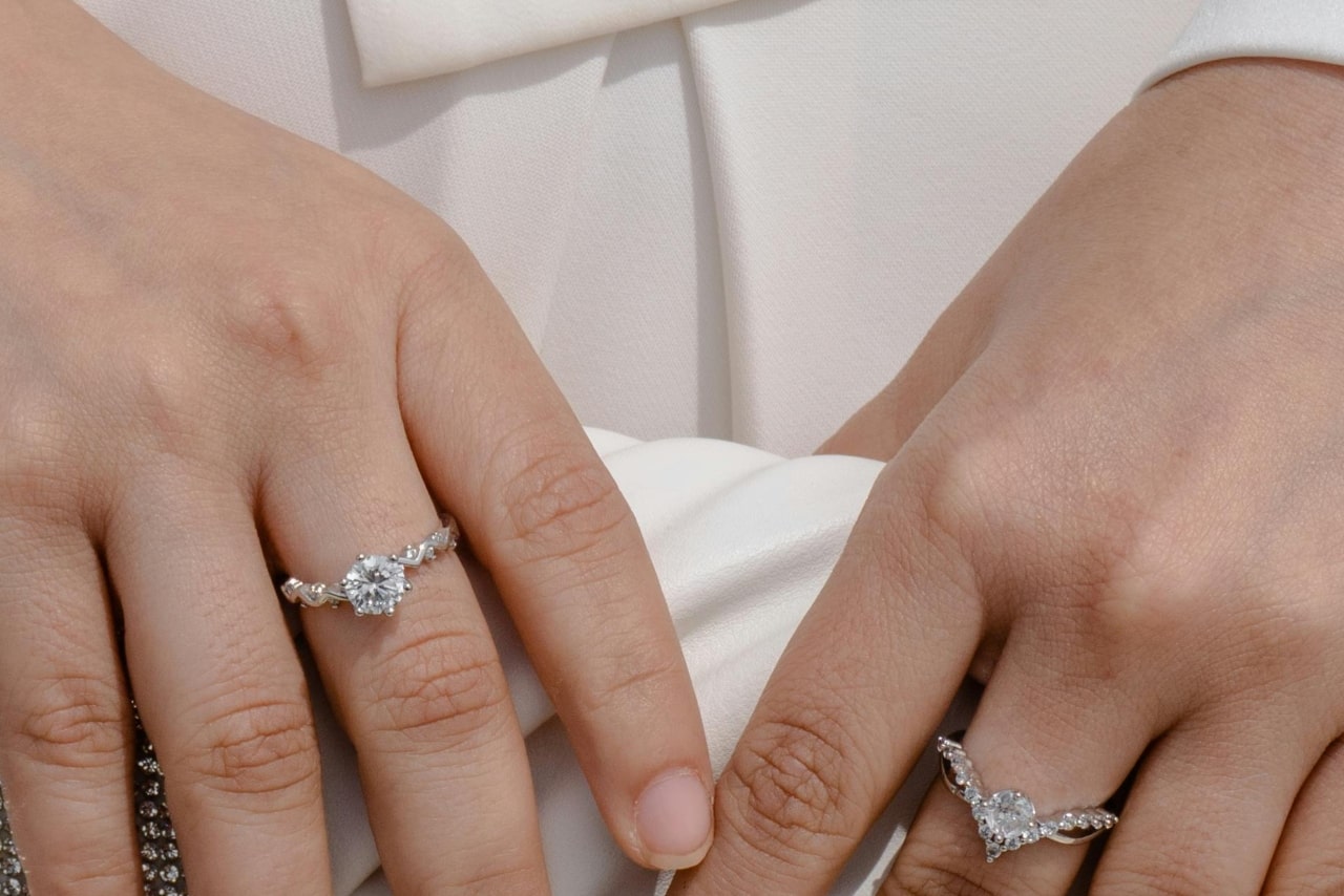 A woman holding a white clutch showcasing gorgeous diamond rings on both hands. A woman holding a white clutch showcasing gorgeous diamond rings on both hands.