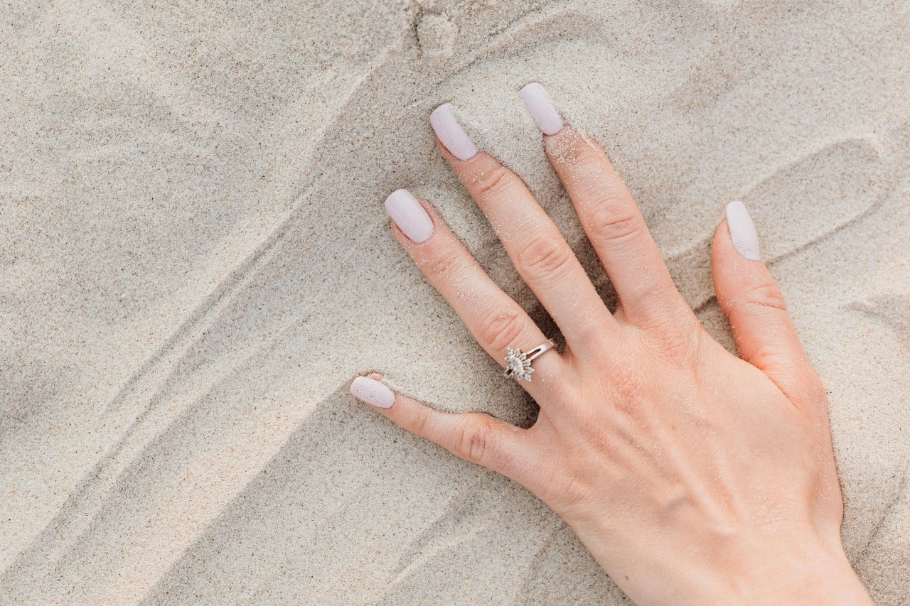 close up of woman's hands on a beach sand wearing engagement ring