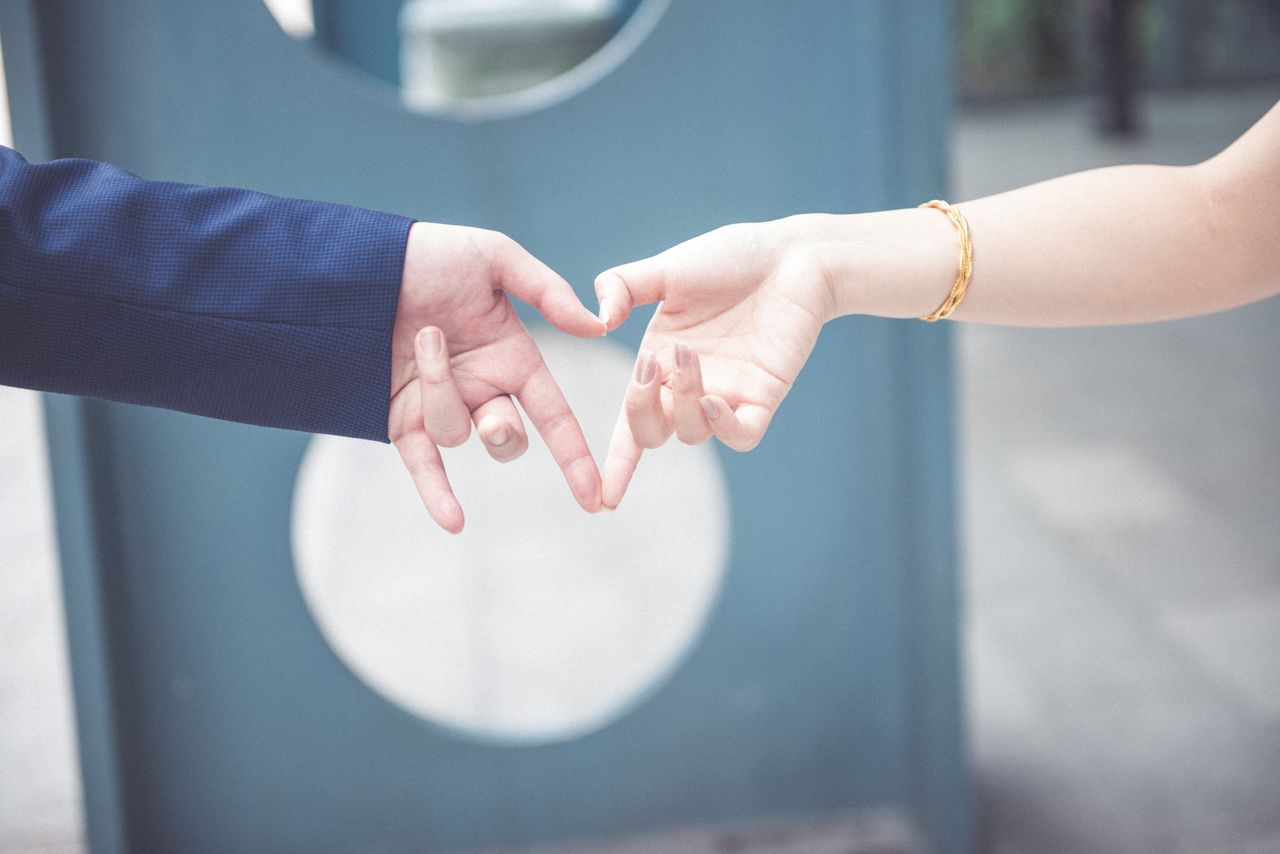A couple making a heart with their hands, showcasing a yellow gold bracelet on the woman’s wrist.